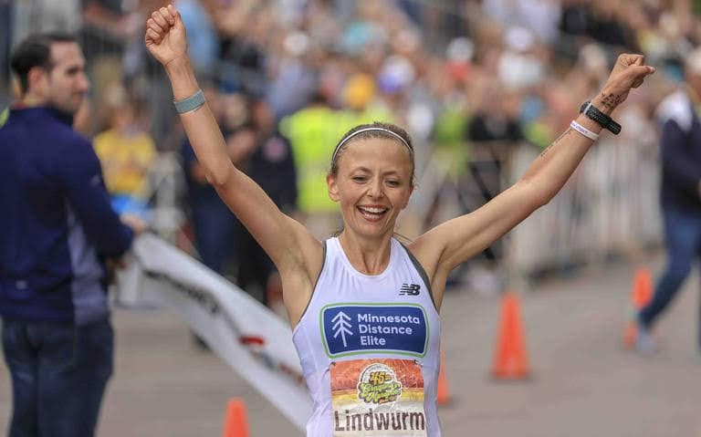 Dakotah Lindwurm reaching finish line with arms raised victoriously in air
