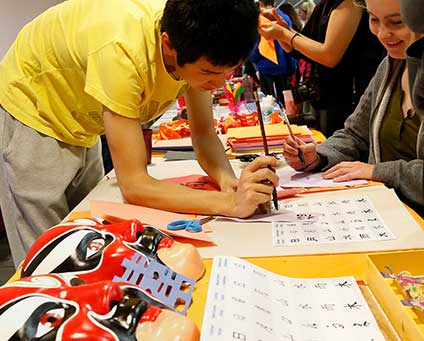 A student in a yellow shirt practices calligraphy at a table