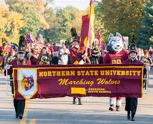 Students carry the NSU Marching Wolves banner at the head of a parade