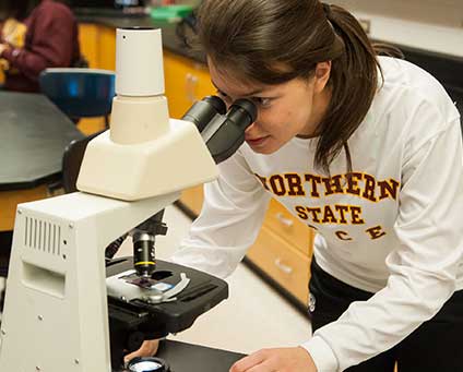 A student in a white Northern shirt uses a microscope in a lab