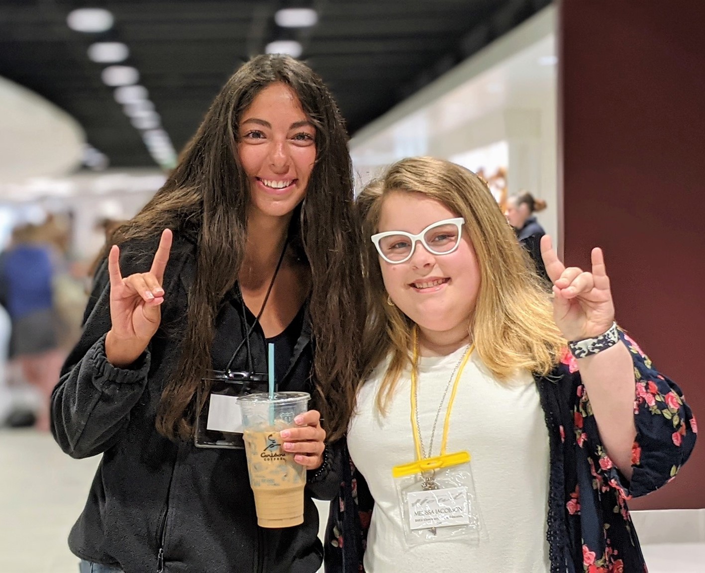Two students smile and make the signature Wolf sign with their hands in the JFAC hallway