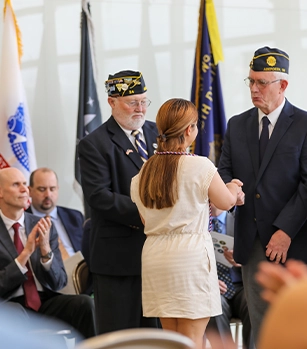 Two members of the American Legion and a female student at the cording ceremony