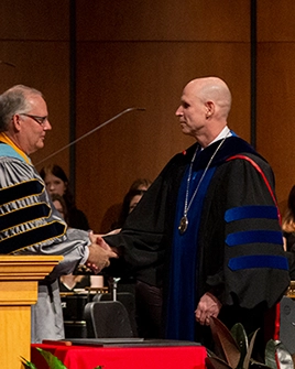 Dr. Neal Schnoor shakes hands with an investiture ceremony attendee