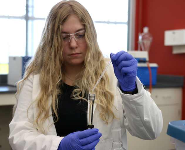 Female student working in lab with piping and glass test tube