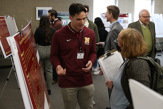 Male student discussing research poster with judge