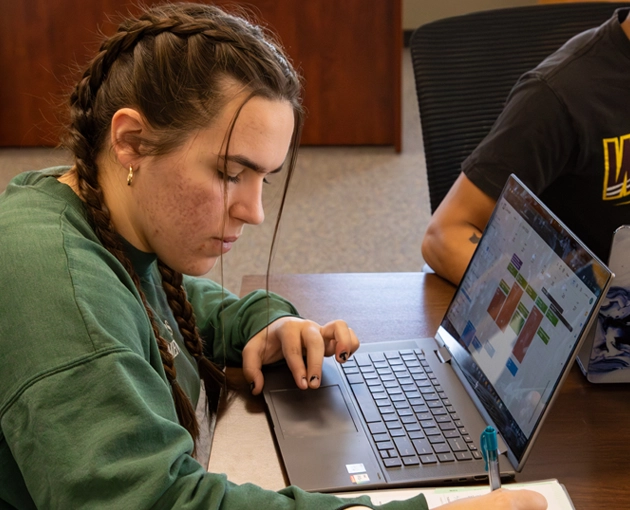 Student working on a laptop and writing notes