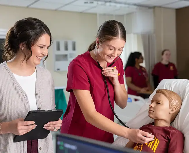 Nursing student using stethoscope on manikin