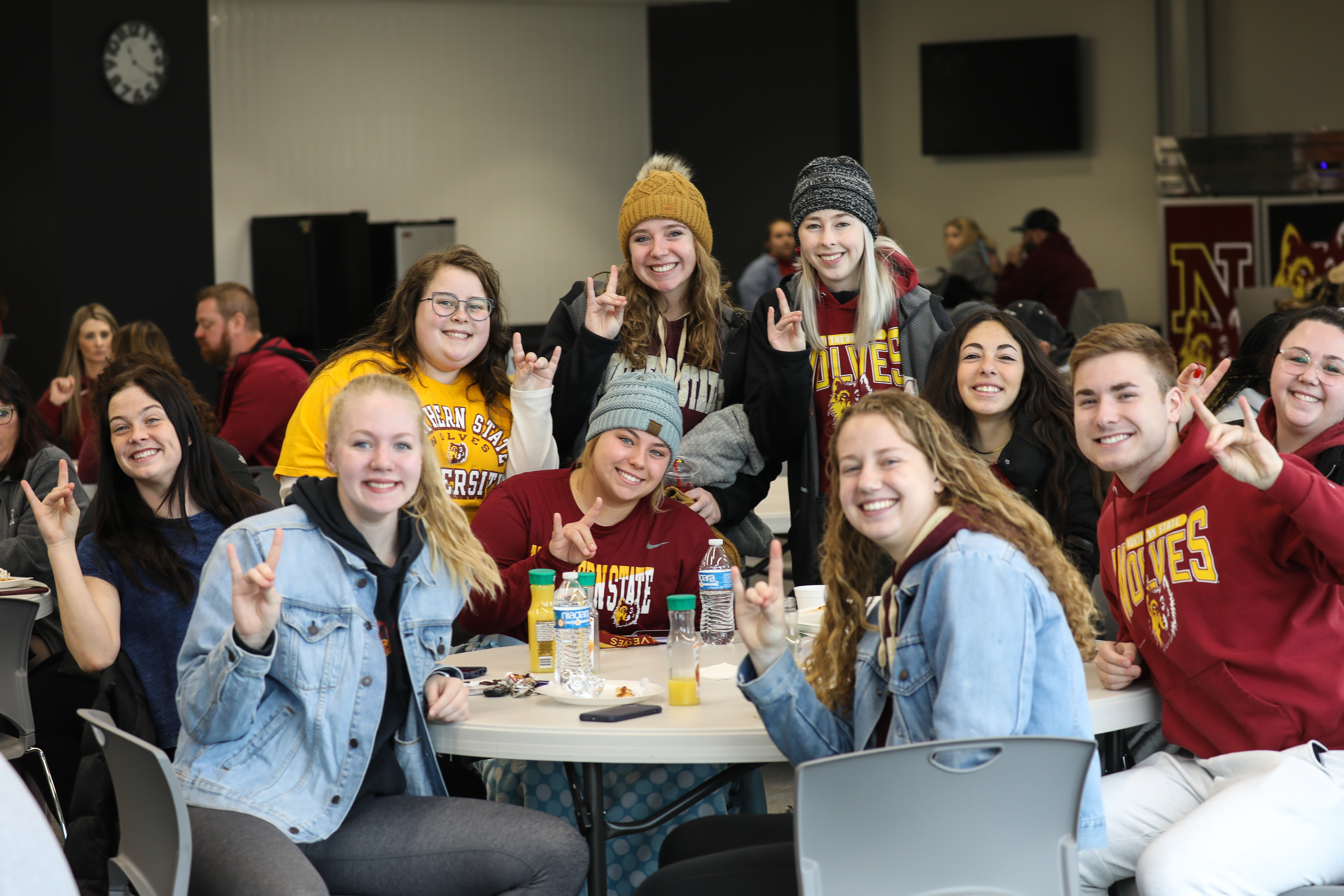 College students in NSU Wolves apparel making the wolf hand signal sitting at a table in Kessler's Champions Club.