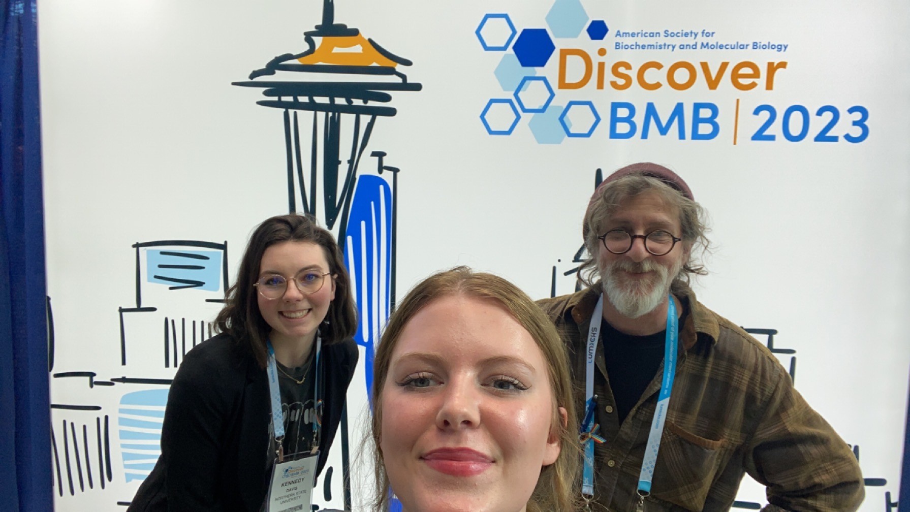 A selfie of students Kennedy Davis and Grace Kramer with Dr. Jon Mitchell in front of the ASBMB 2023 Conference sign