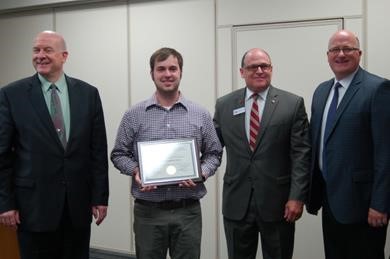 Corey Klatt stands smiling with award among important BOR and NSU representatives