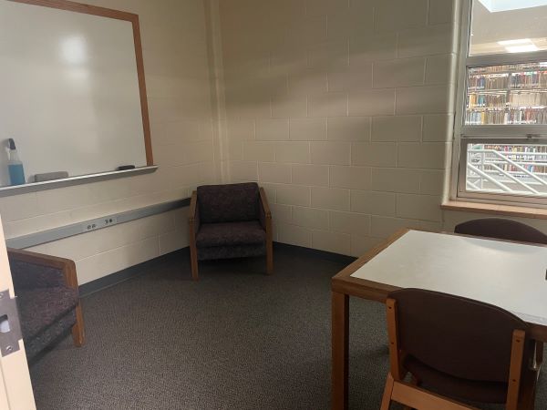 Chairs, a table, and a whiteboard in a room with light walls, brown carpet, and a window