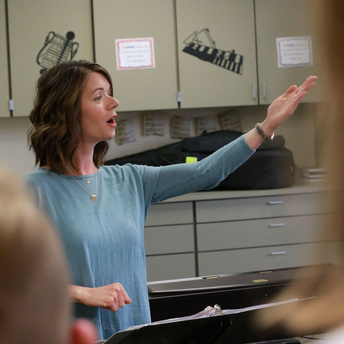 A music teacher in a blue shirt gestures to the class