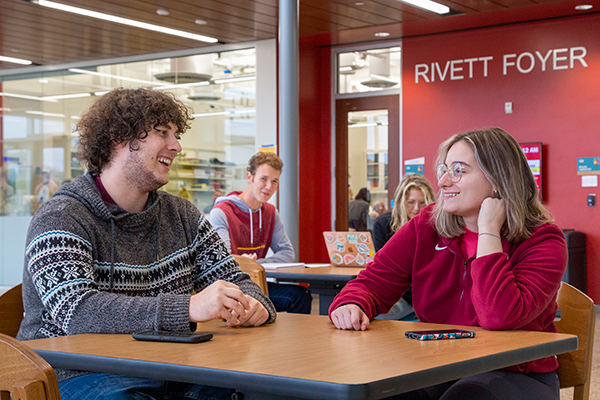 Smiling students are seated together at tables in the Jewett Science Center's Rivett Foyer