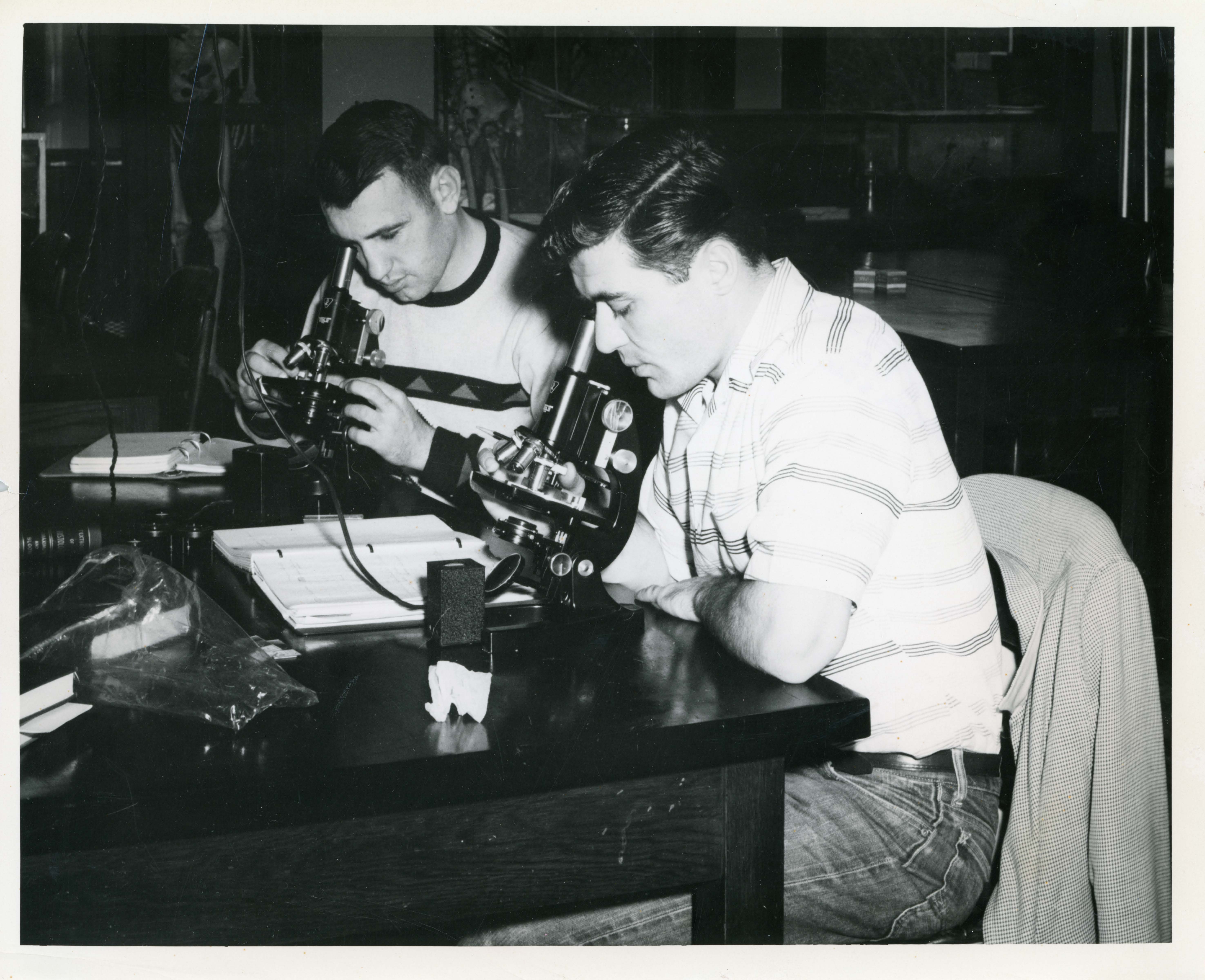 Historic photograph of two scientists sitting at a desk and looking through microscopes