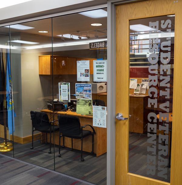 The glass front of the Student Veteran Resource Center in Avera Student Center with desk and chairs