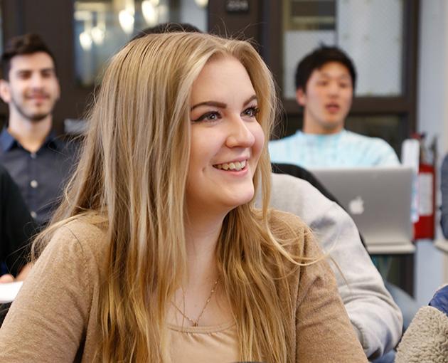 A student with long blonde hair smiles in class
