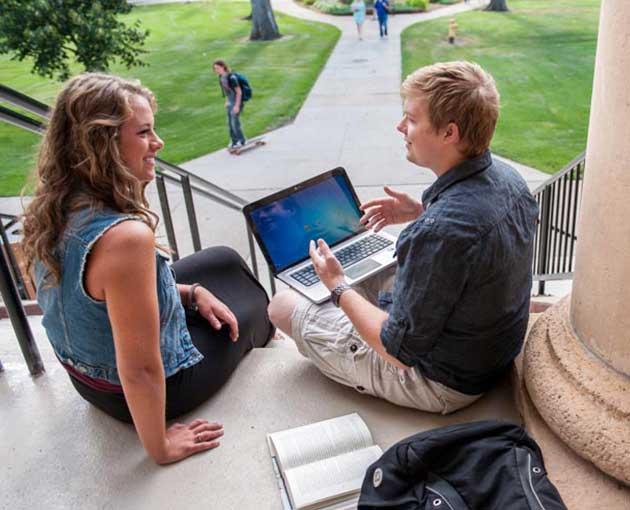 Two students chat at the top of a flight of stairs leading to the campus green
