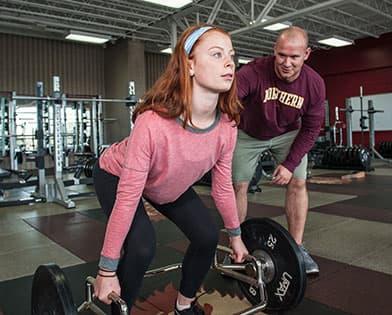 Female lifting weights with coach beside her