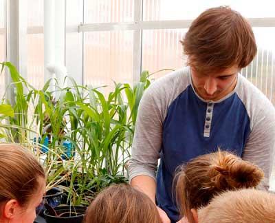 A student demonstrates for children in a greenhouse