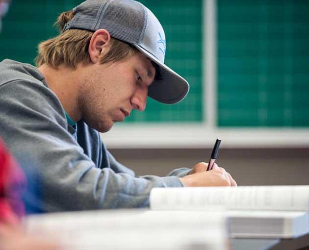 A student in a cap leans over papers in a classroom