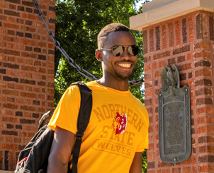 Student in NSU attire smiling outside on campus