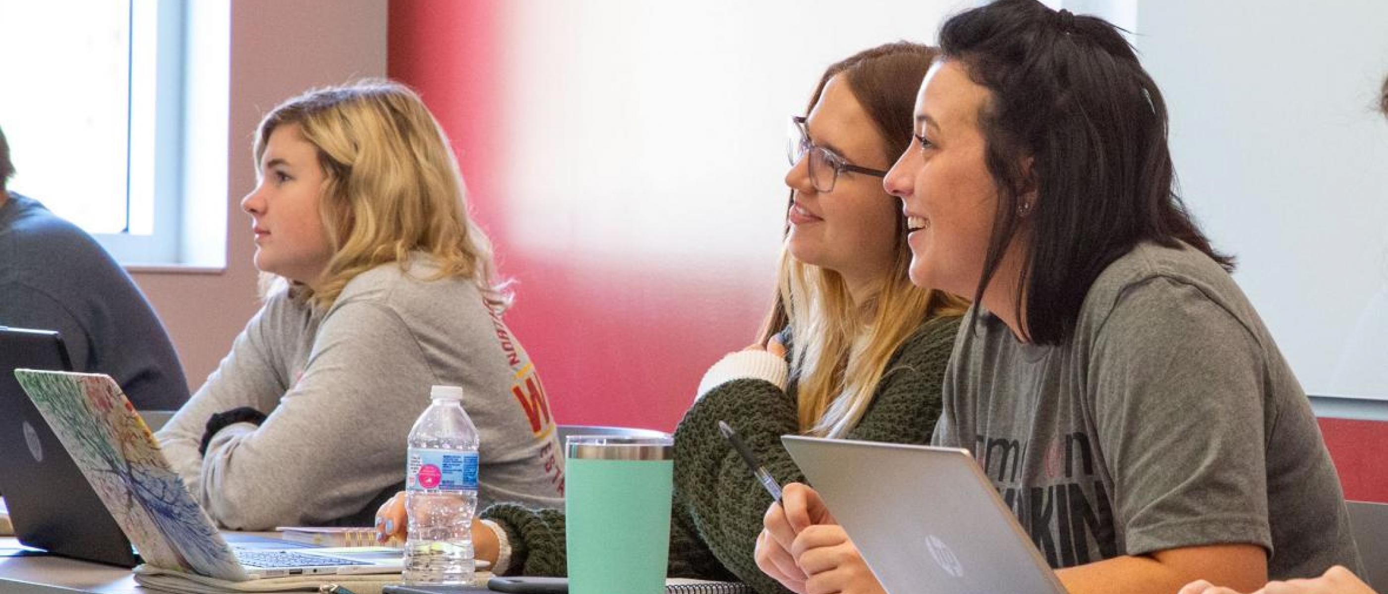Three students with laptops are attentive in class