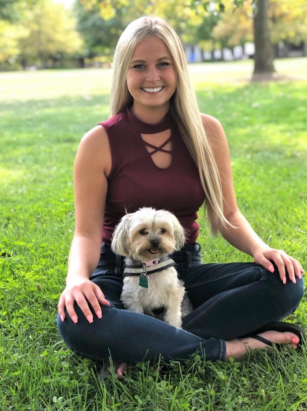 Photo of young woman sitting on grass with small dog