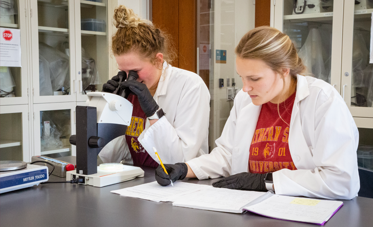 Two female college students in white coats working in a lab