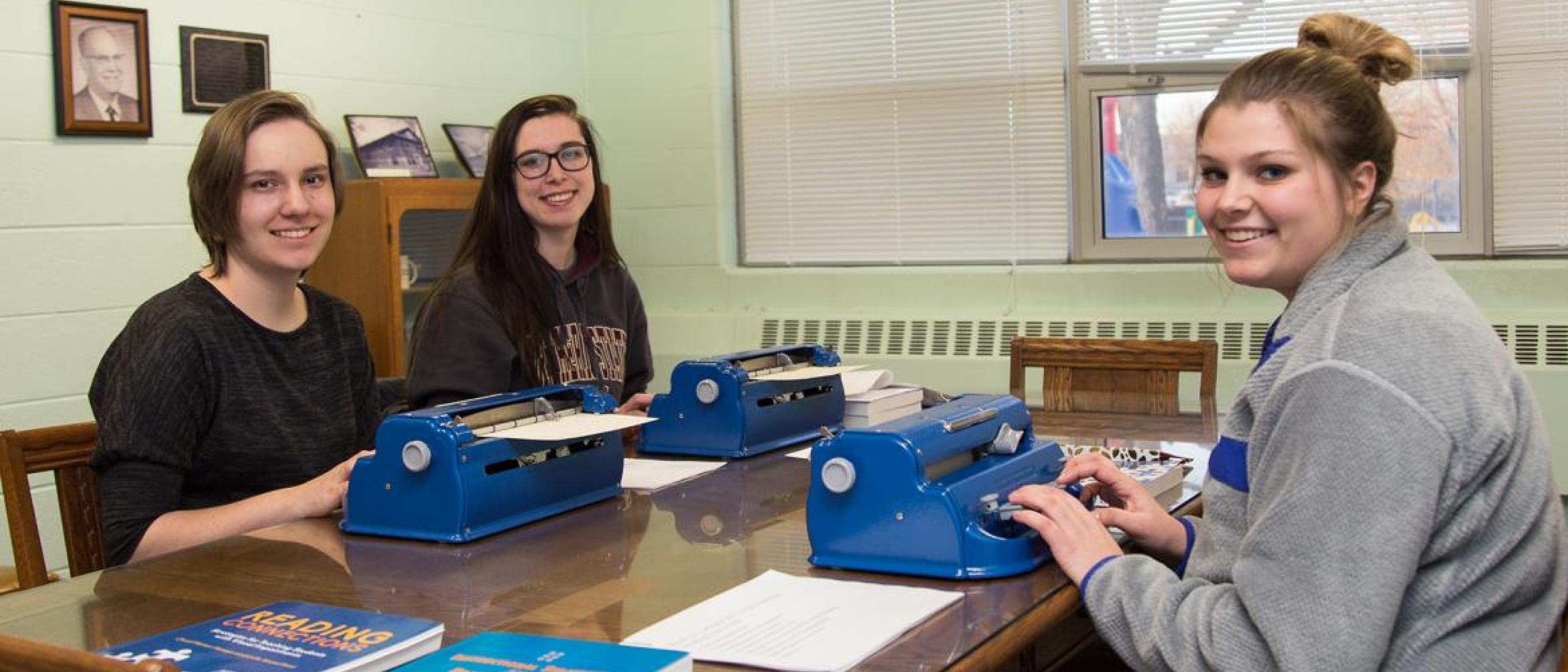 Three students smiling and using braille typewriters