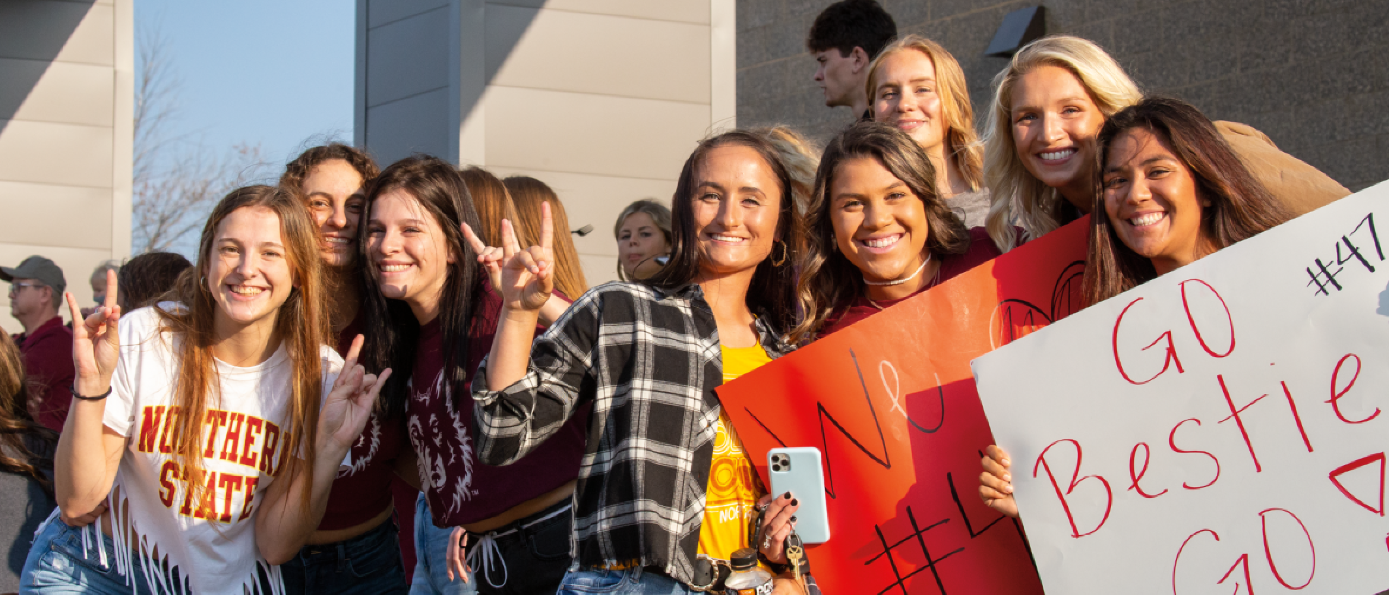 Smiling students in Northern clothing outside hold a sign that says "Go Besties"