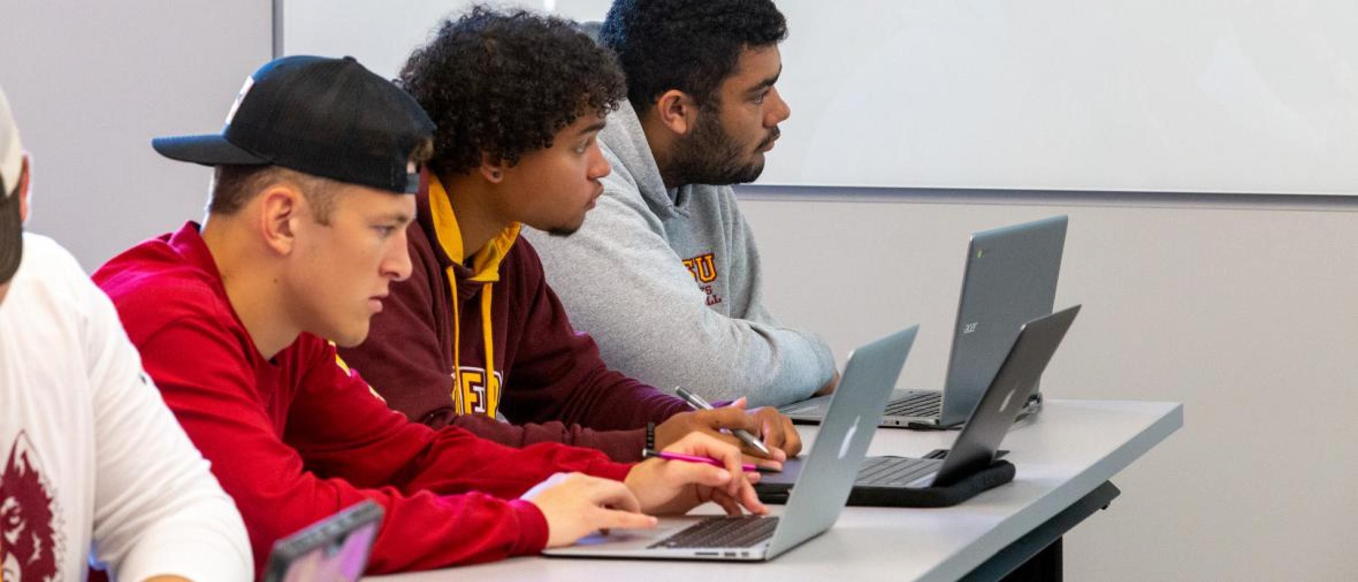 Three students with laptops are attentive in class