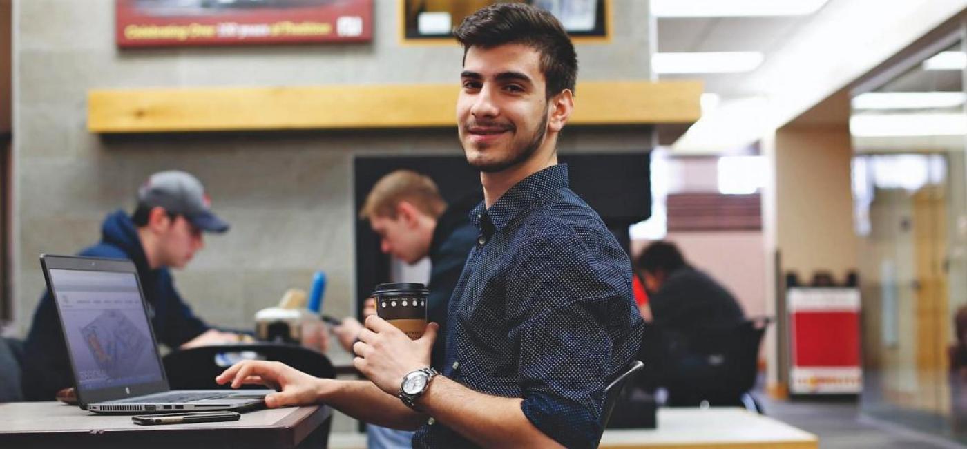 Student holding coffee and working on laptop