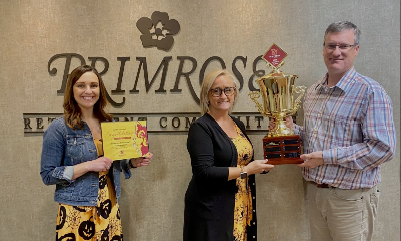 Three people holding awards stand in front of a Primrose sign on a wall