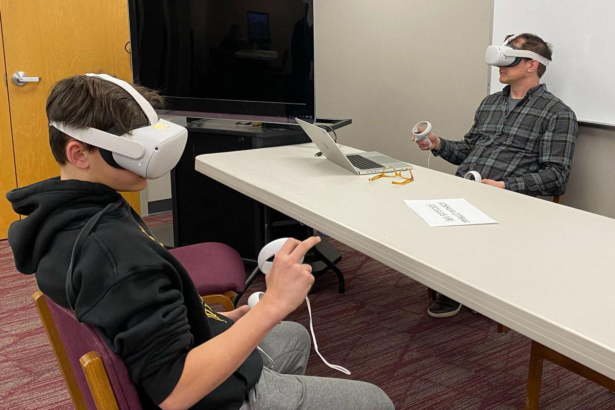 Two peple wearing VR headsets seated at a table