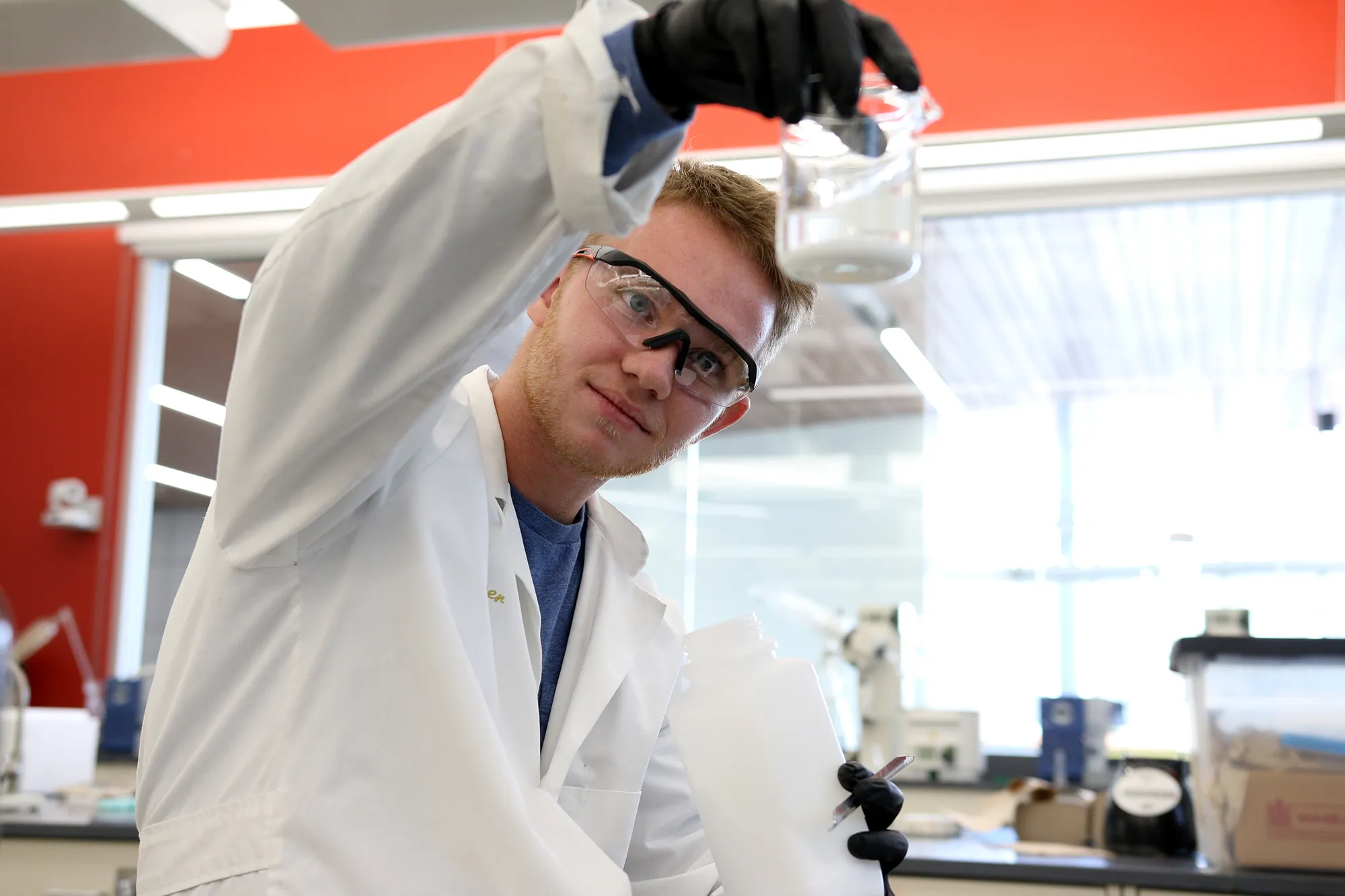 A student in goggles examines a jar in a lab