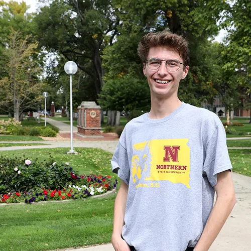 Jaron Gross smiling and standing in front the campus green