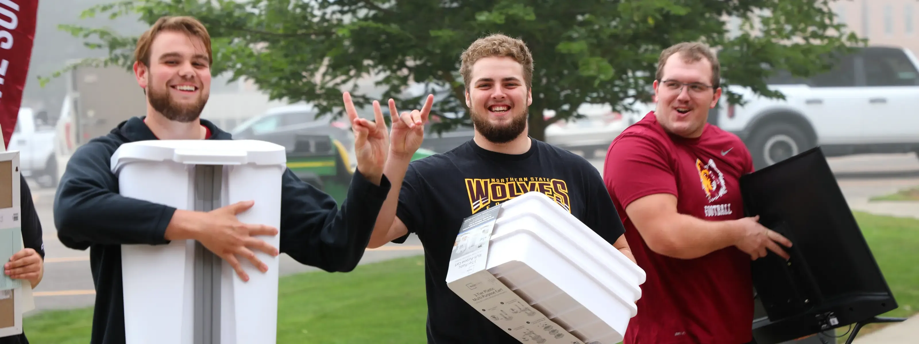 A father and two students moving items into the residence halls wearing NSU spirit attire.