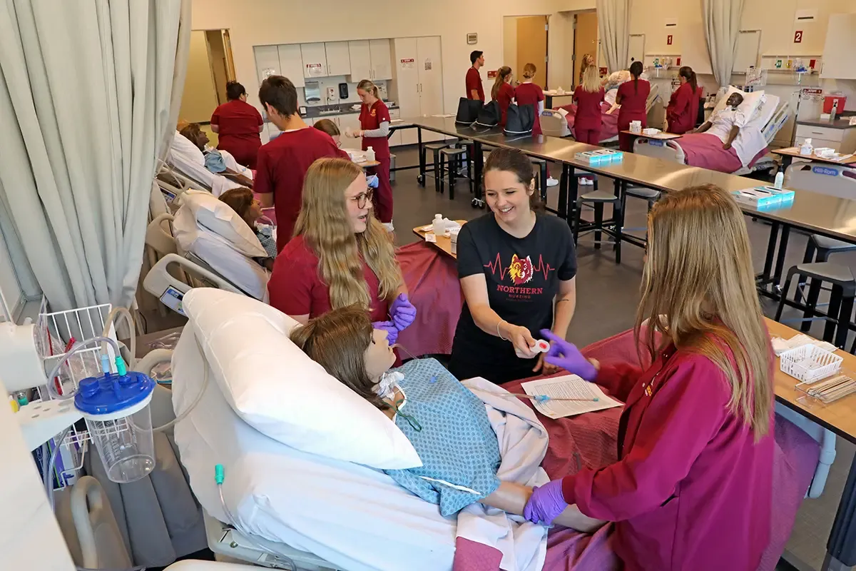 Nursing students working in the simulation lab around hospital beds