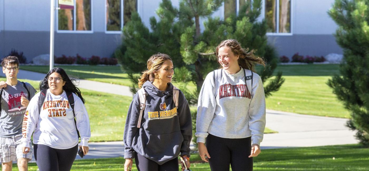 Students in sweatshirts smile at each other as they walk across campus