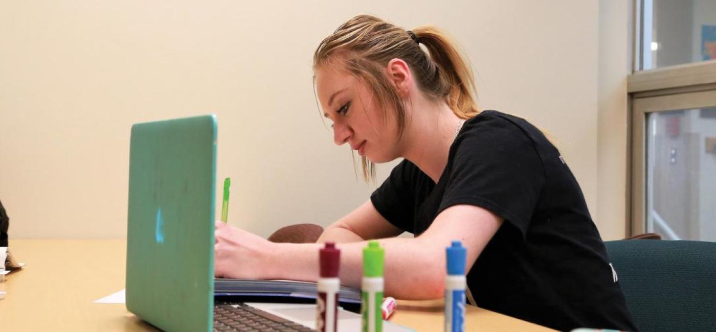 A seated student studies near a laptop