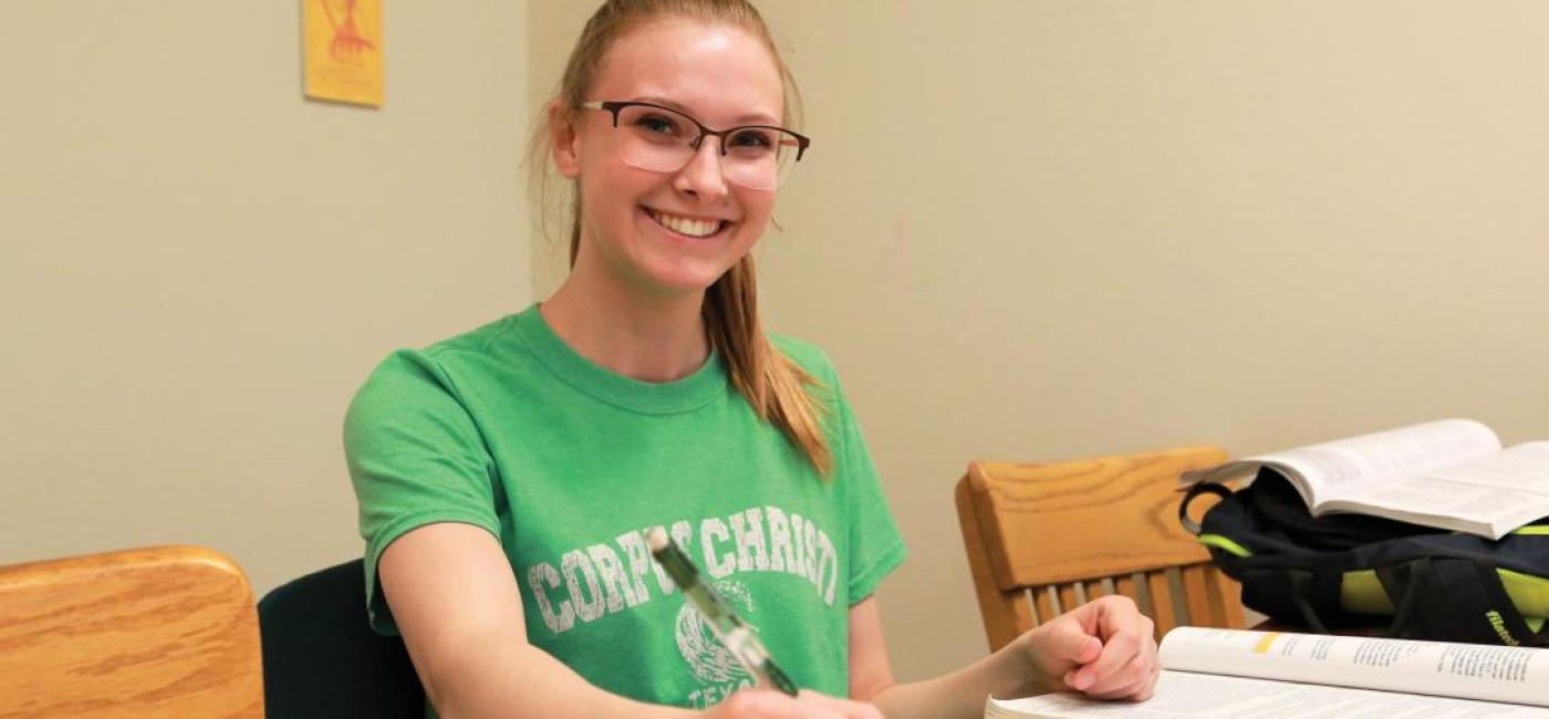 A student with glasses in a green shirt works at a table