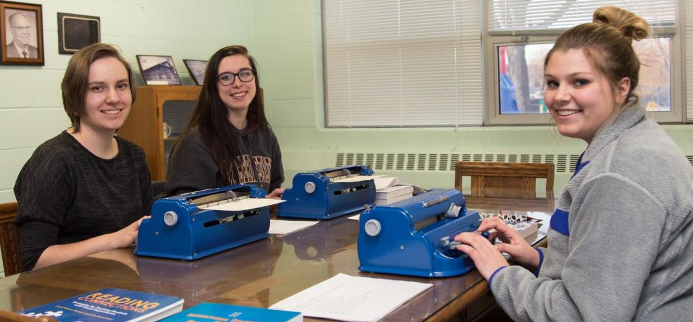 Three students smiling and using braille typewriters