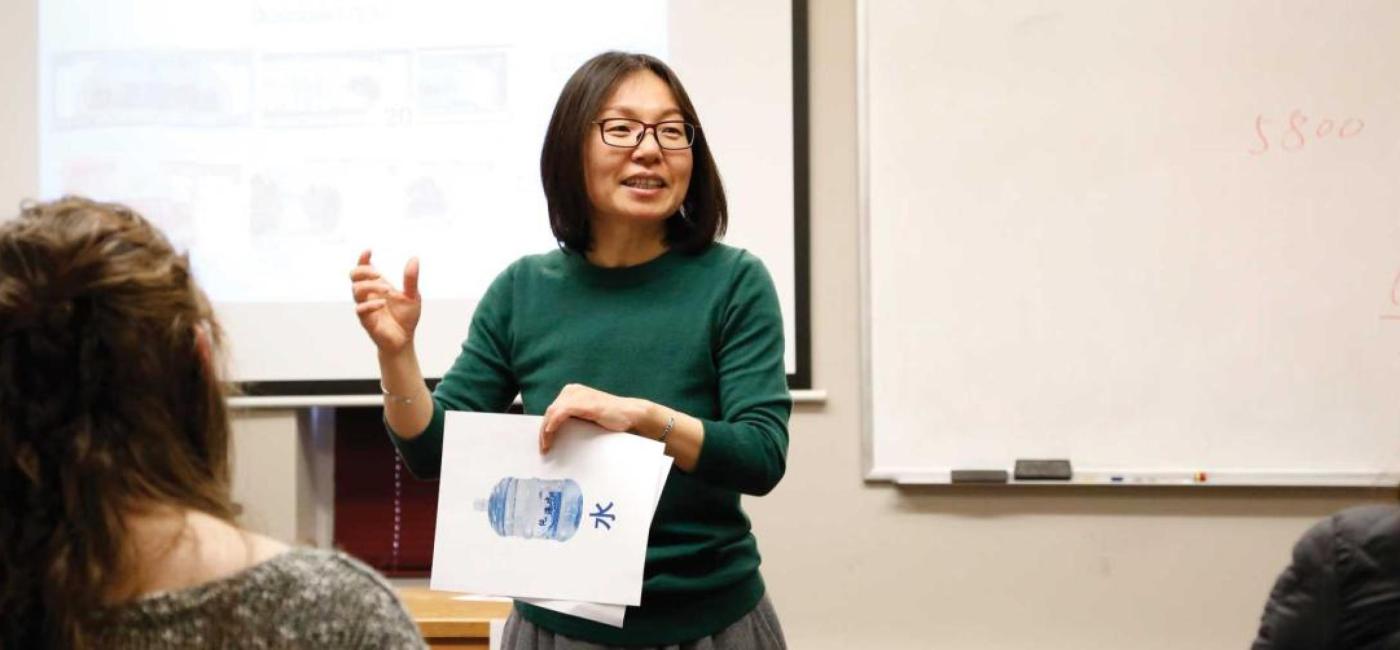 An instructor in a green sweater and black glasses shows pictures to a class