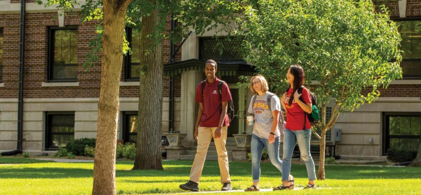 Three students smiling and walking to class together on campus green