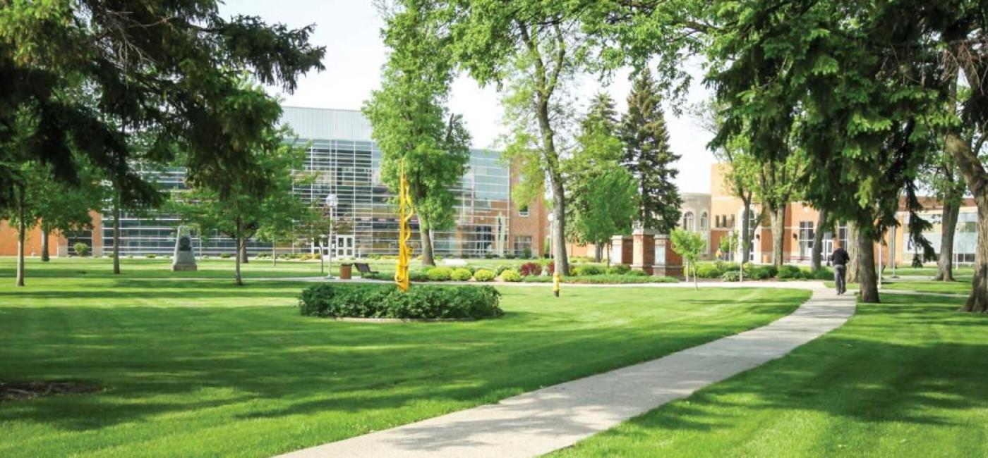 Photo of campus green with trees and buildings in the background