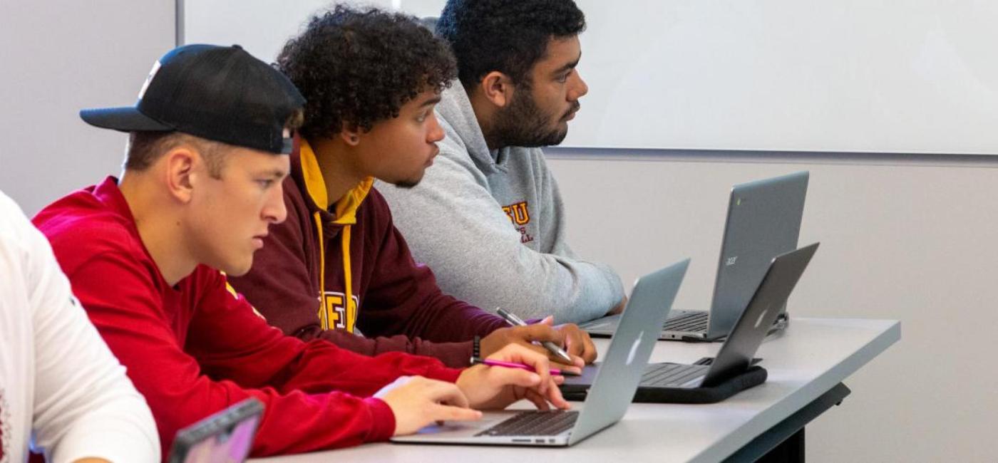 Three students with laptops are attentive in class