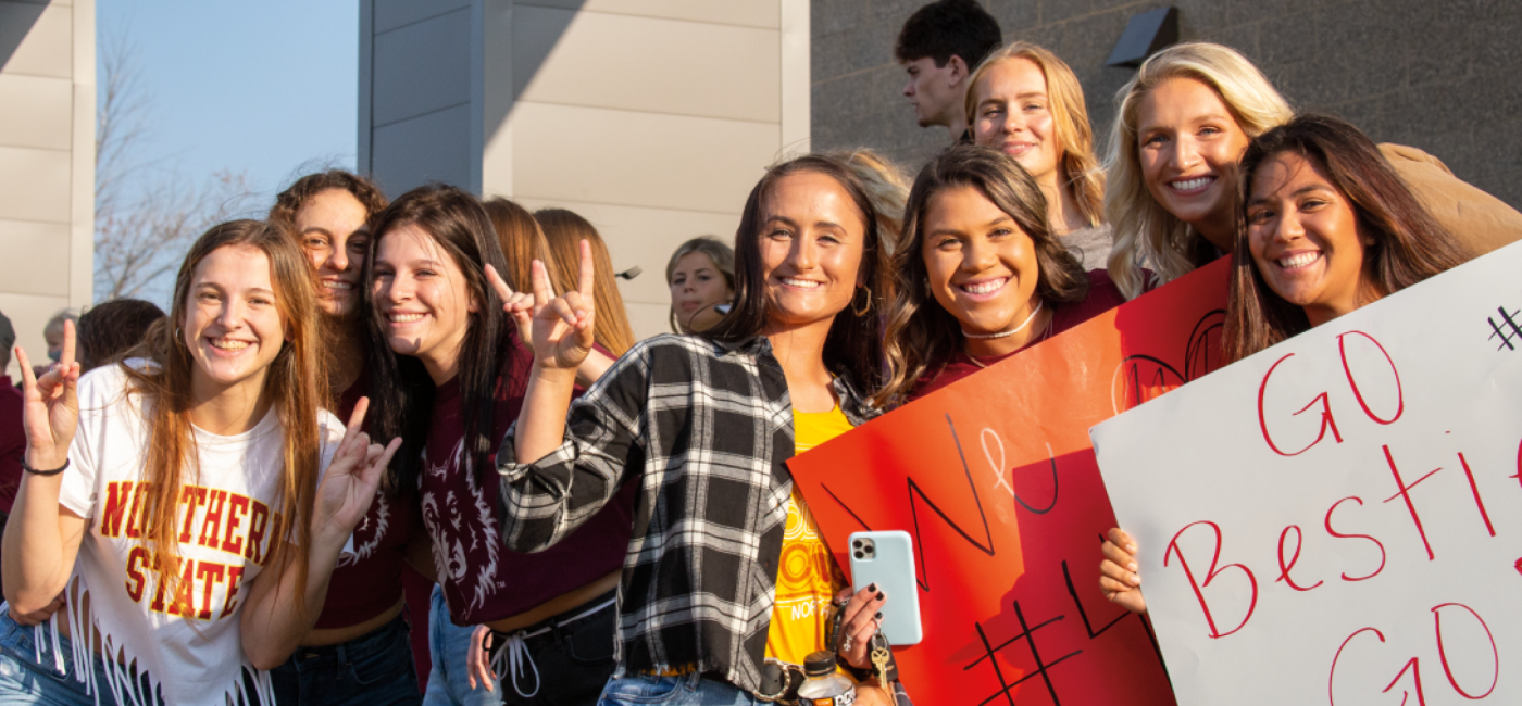 Smiling students in Northern clothing outside hold a sign that says "Go Besties"