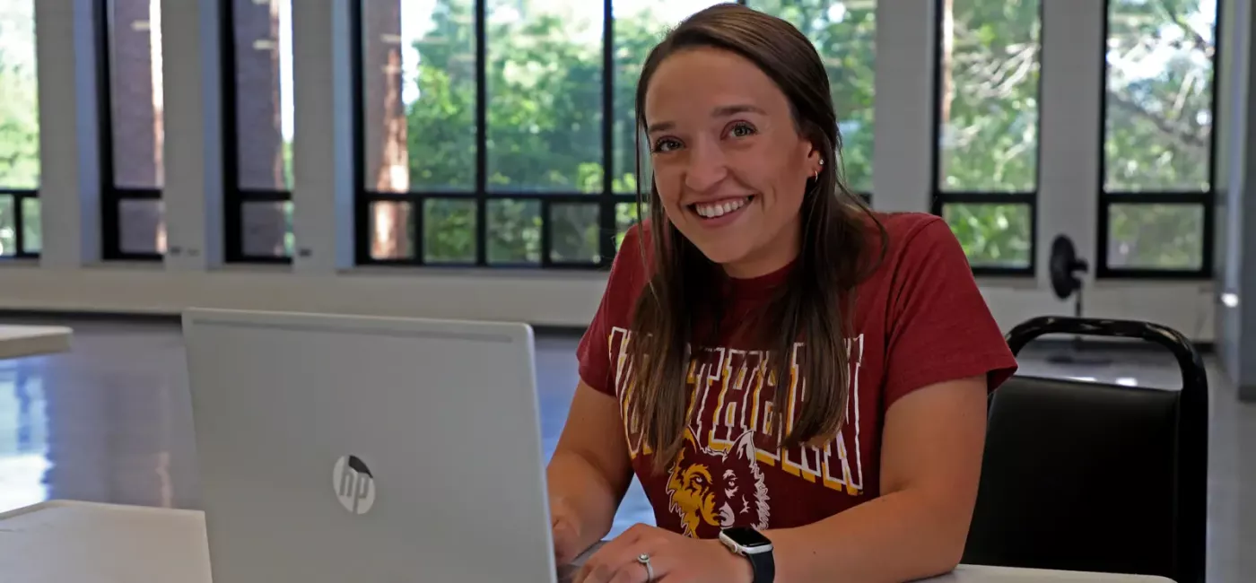 A smiling student in a classroom looks up from her laptop