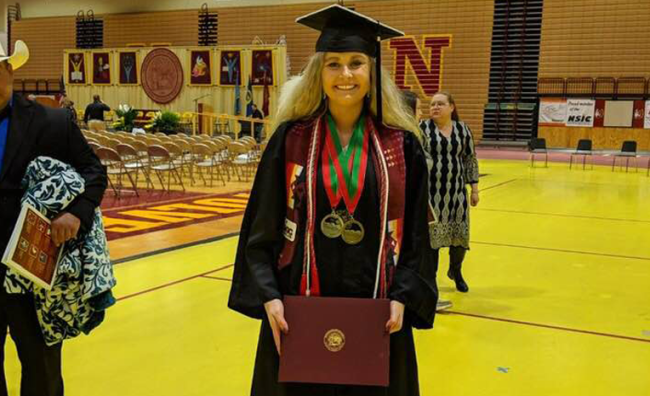 College student standing in cap and gown at commencement holding degree