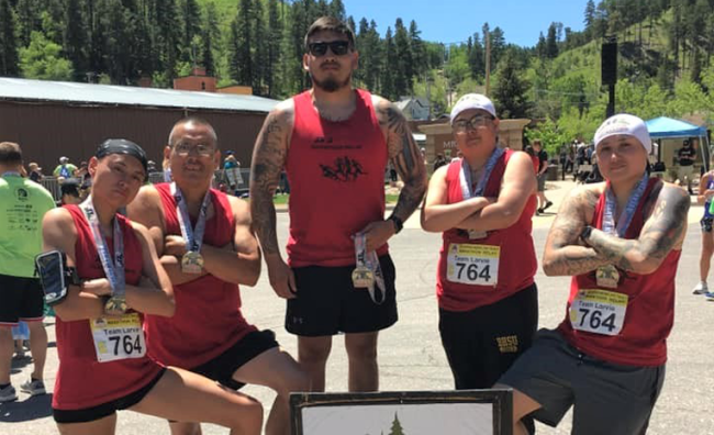 A family standing with arms crossed after a race against a blue sky and mountain background